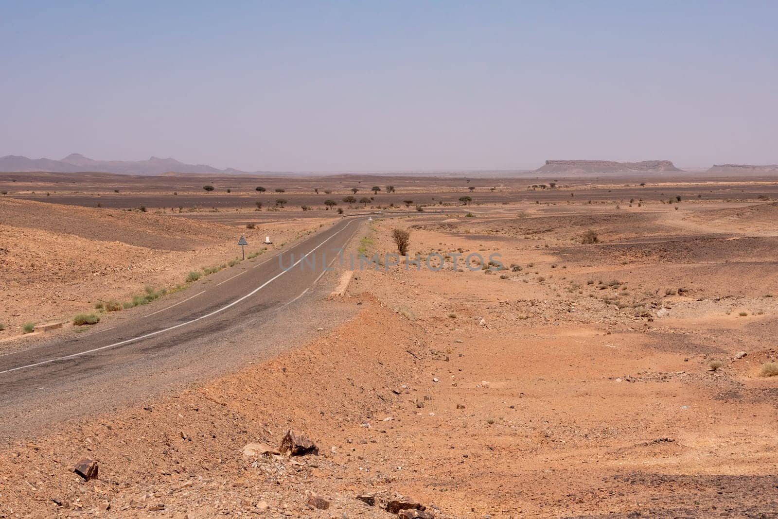 A road leading through the desert near Merzouga, famous horseshoe mountain Gara Medouar in the background, Morocco