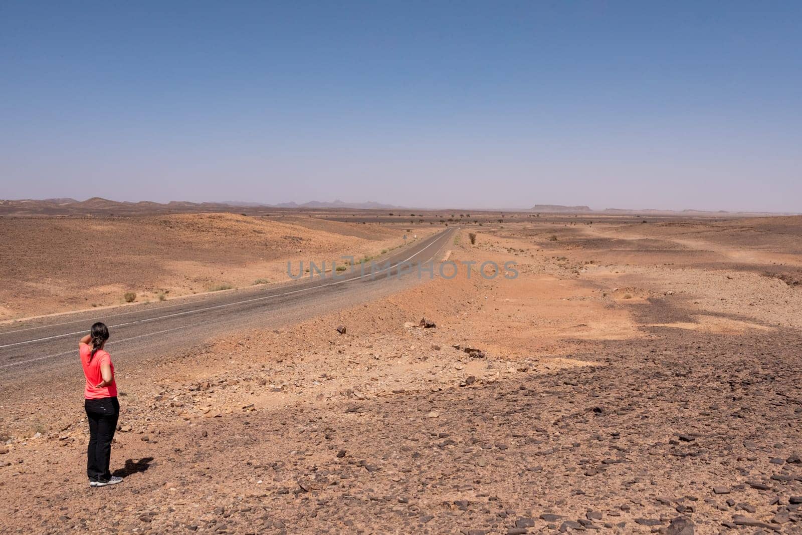 A road leading through the desert near Merzouga, famous horseshoe mountain Gara Medouar in the background, a tourist enjoying the view, Morocco