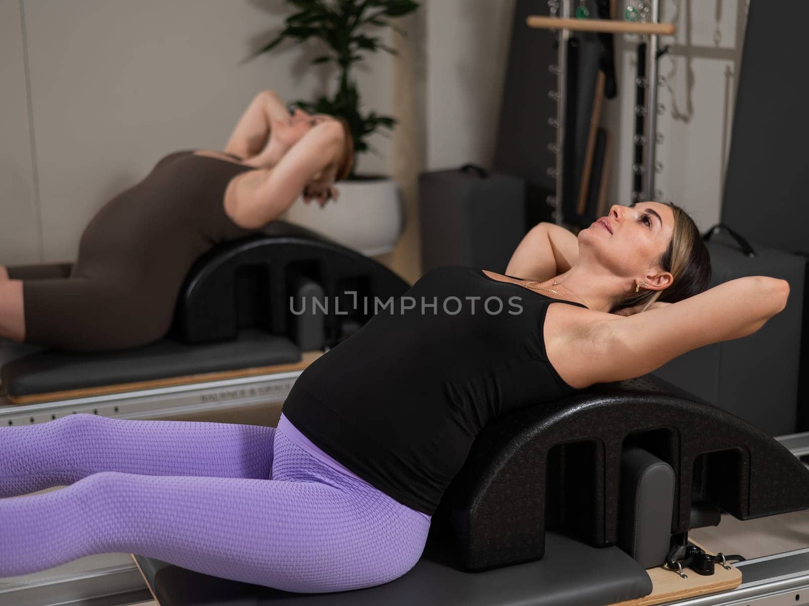 Two pregnant women do Pilates exercises on a reformer. Yoga class for pregnant women