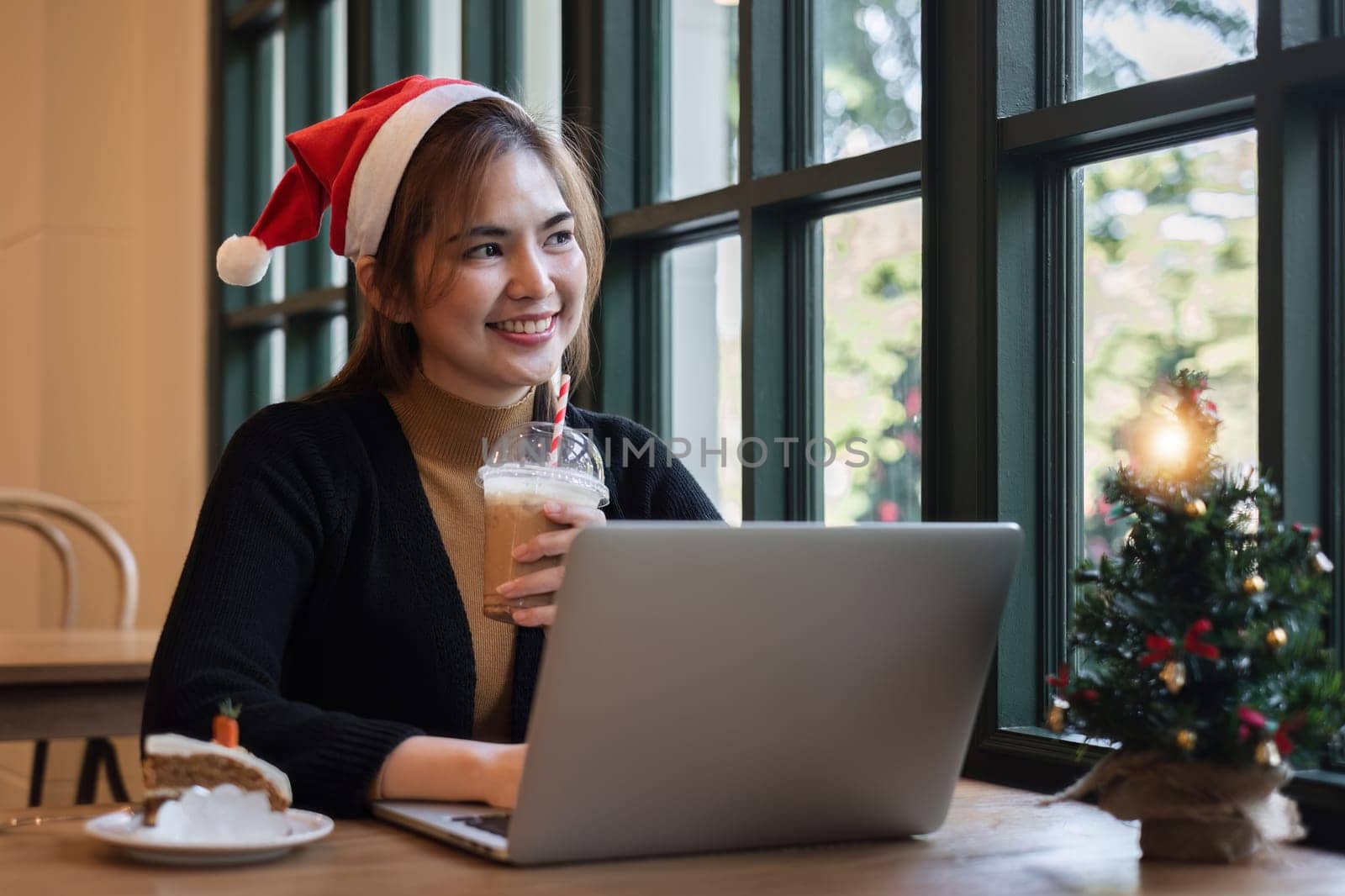 A businesswoman sits and work using a laptop in an office decorated with a Christmas tree and colorful lights during the holiday season. Spend Christmas at work.
