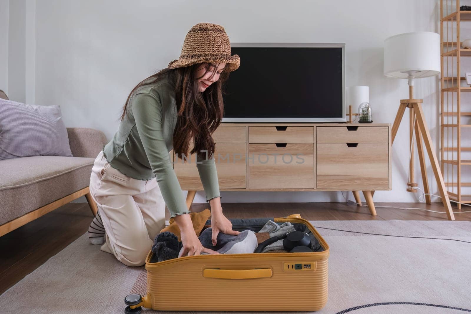 Beautiful Asian woman try to pack clothes into a yellow suitcase to prepare for a weekend getaway. by wichayada