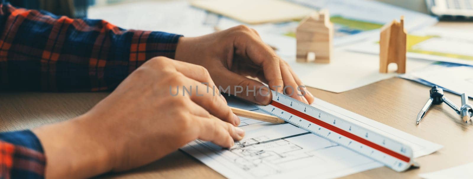 Closeup of architect engineer hand using ruler to mature and draw a blueprint on meeting table with wooden block, pencil and blueprint scatter around at architectural modern office. Delineation.