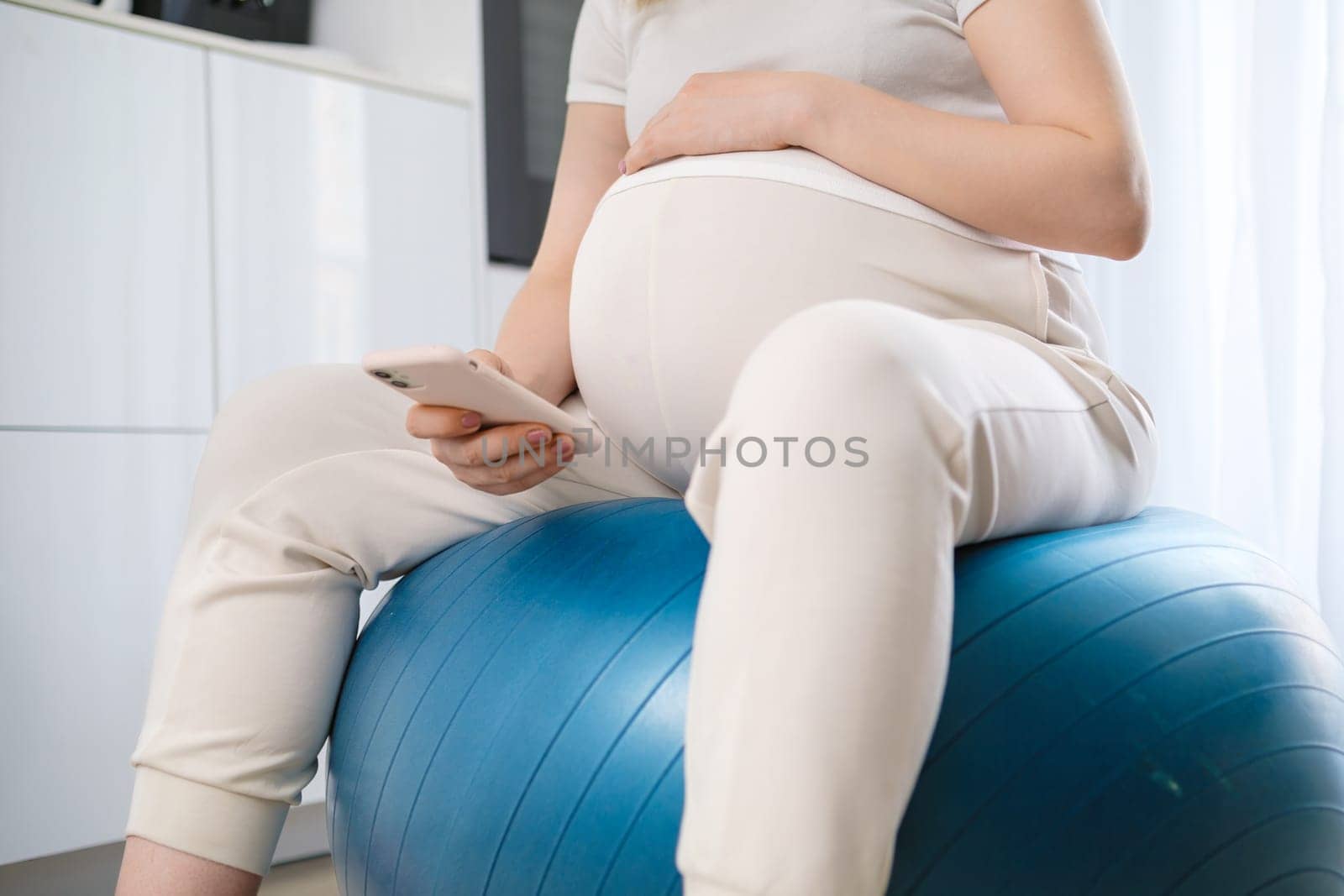 Pregnant woman uses a mobile phone while sitting on the fit ball.