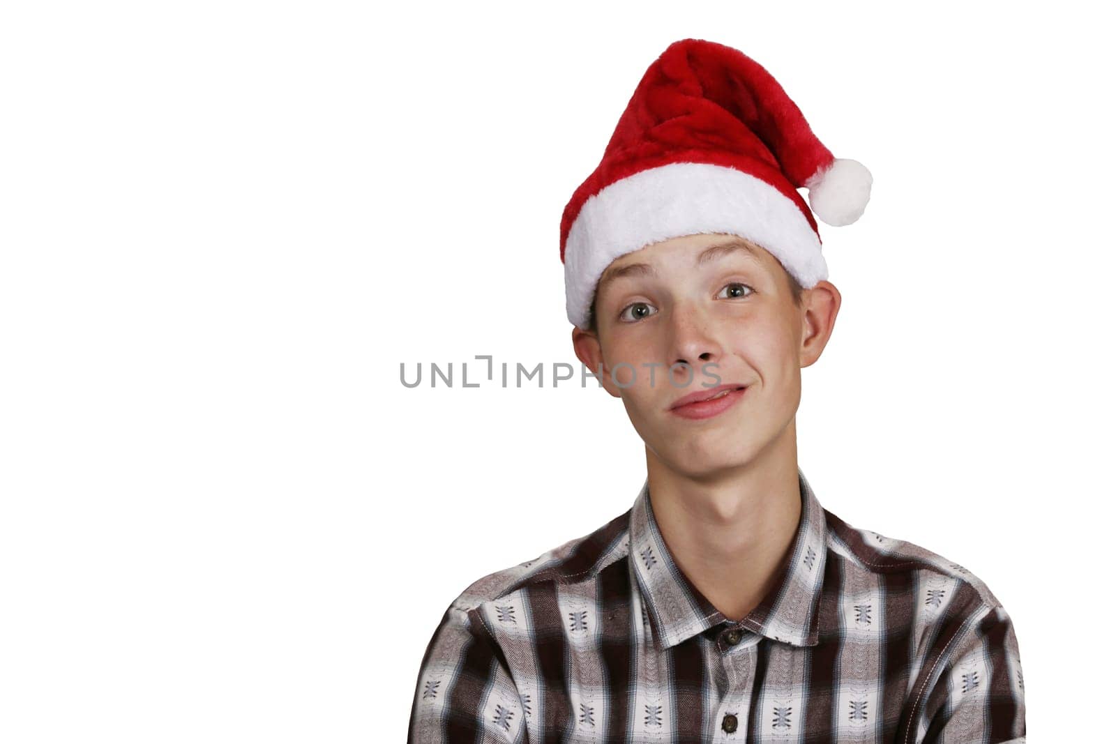 Funny, charismatic teenage boy in a shirt, wearing a Santa Claus hat, on a white isolated background. The boy makes a grimace.