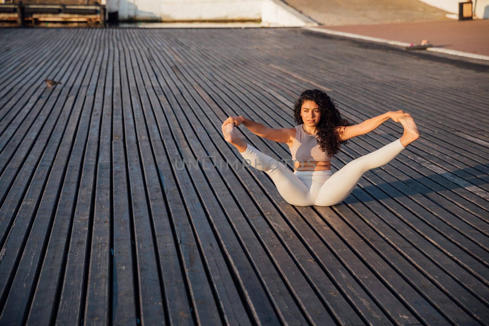 Full length portrait of a middle aged woman doing yoga or pilates on a mat outside in a park.Pose chakravakasana. by Simakov