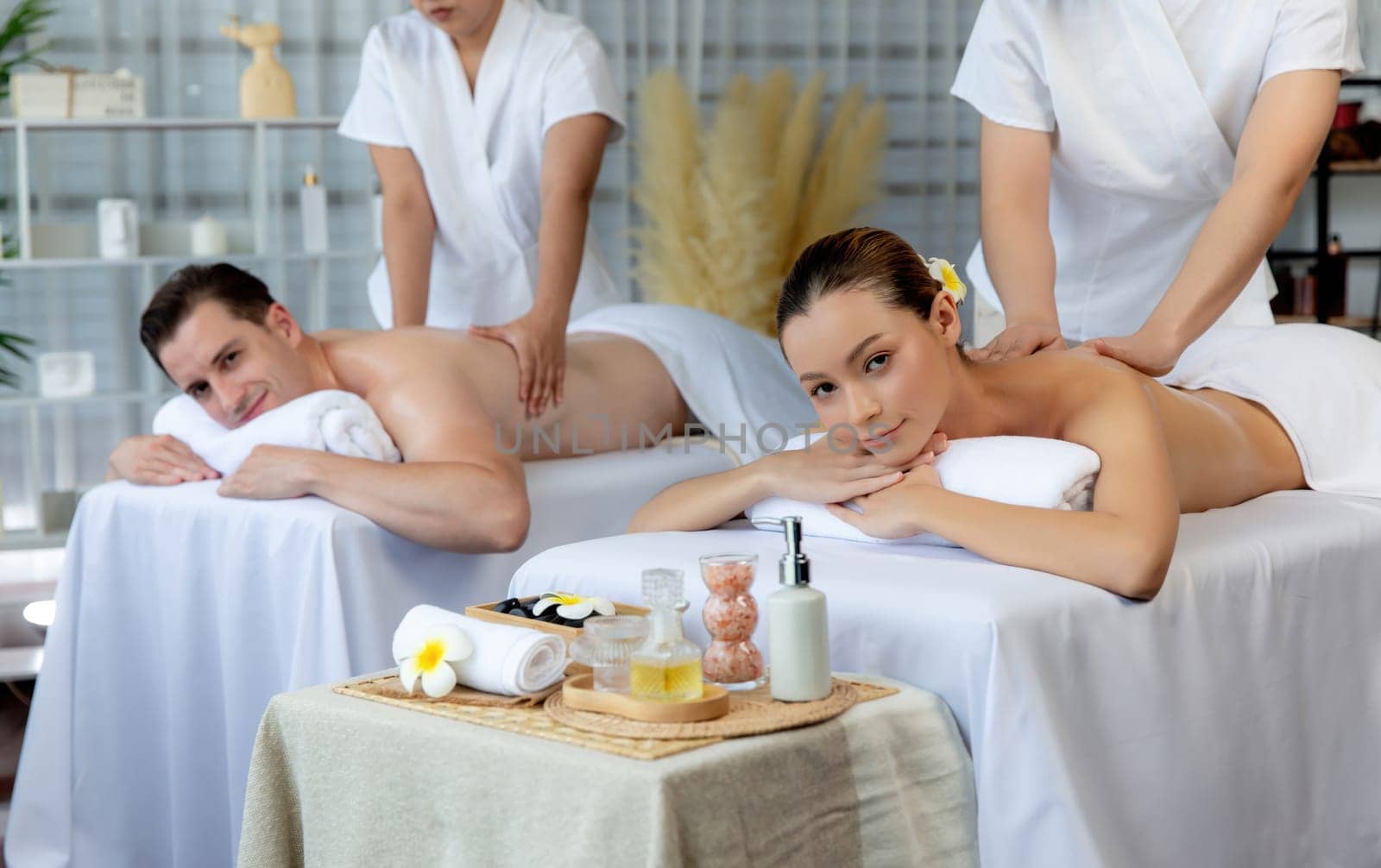 Caucasian couple customer enjoying relaxing anti-stress spa massage and pampering with beauty skin recreation leisure in day light ambient salon spa at luxury resort or hotel. Quiescent