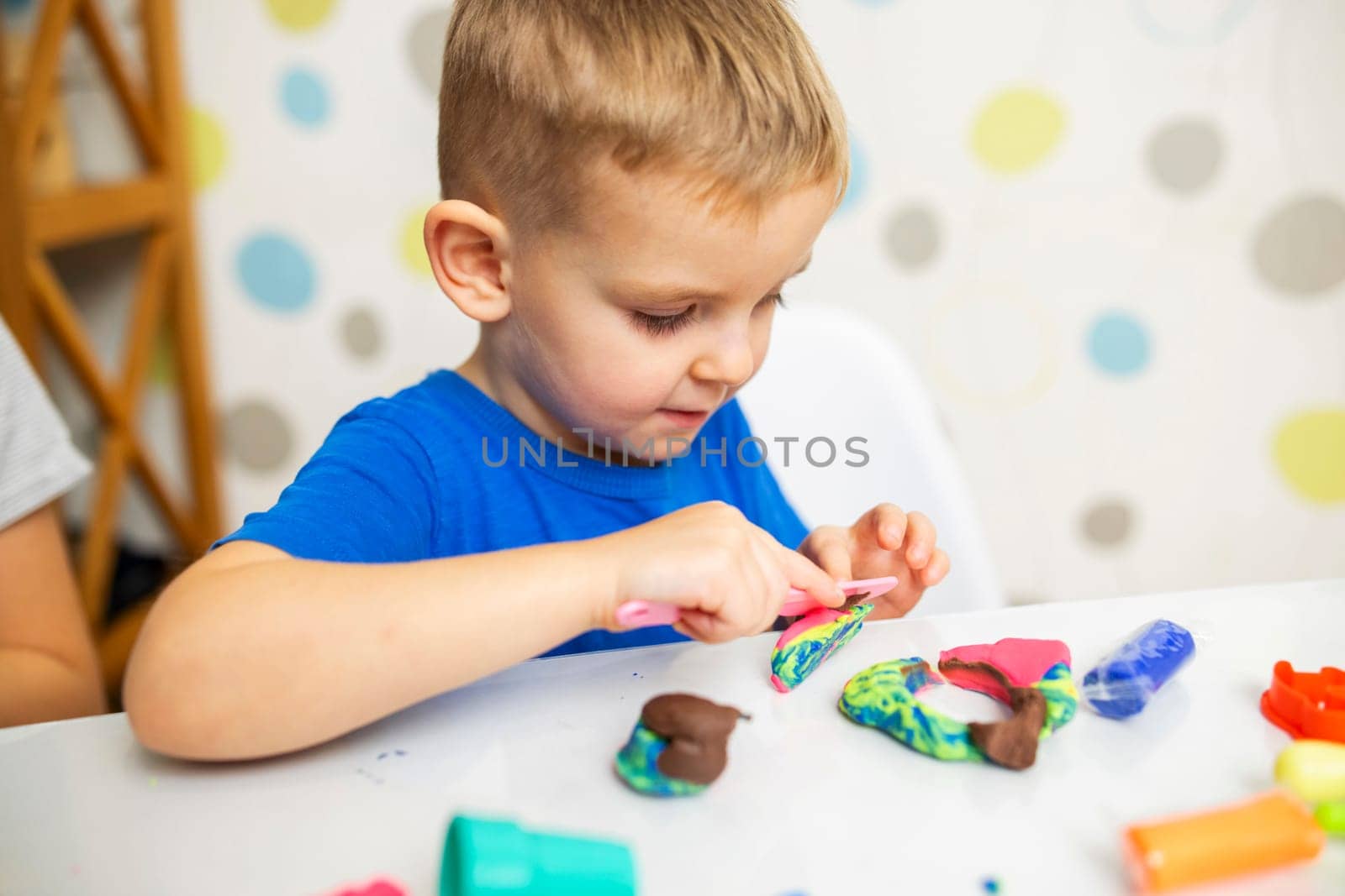 Little boy enthusiastically plays with plasticine, play dough on white table at home, children's creativity concept. Development of fine motor skills