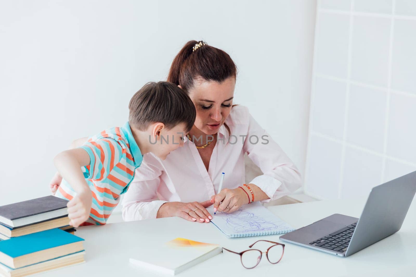 Woman with boy watching online laptop at desk at work in office by Simakov