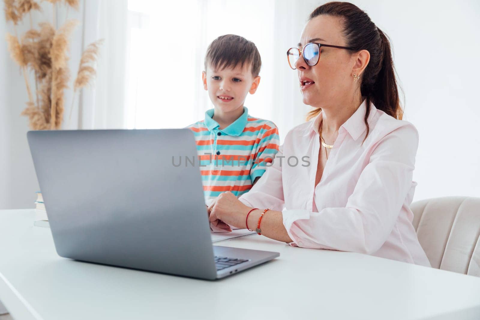 Woman with boy watching online laptop at desk at work in office by Simakov