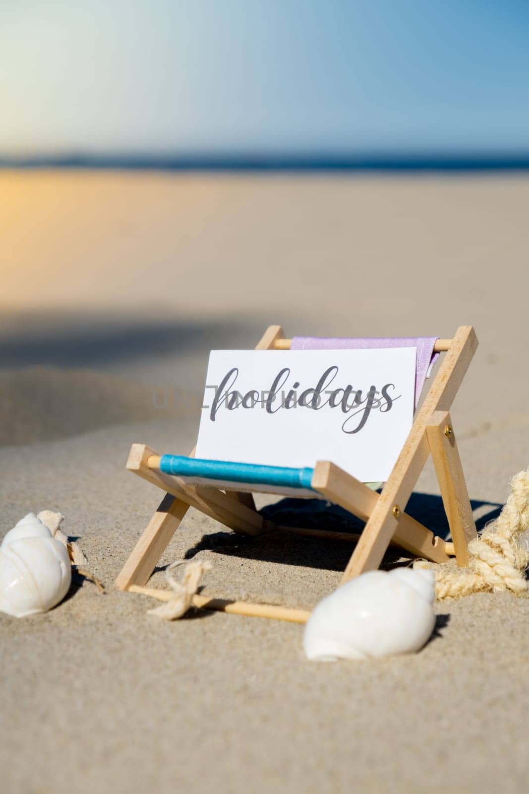 HOLIDAYS text on paper greeting card on background of beach chair lounge summer vacation decor. Sandy beach sun. Holiday concept postcard. Travel Business concept