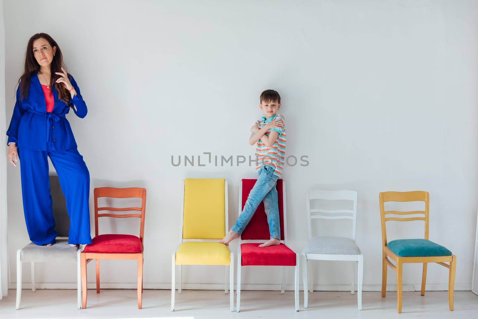 Boy and woman and many different chairs in the interior of a white room