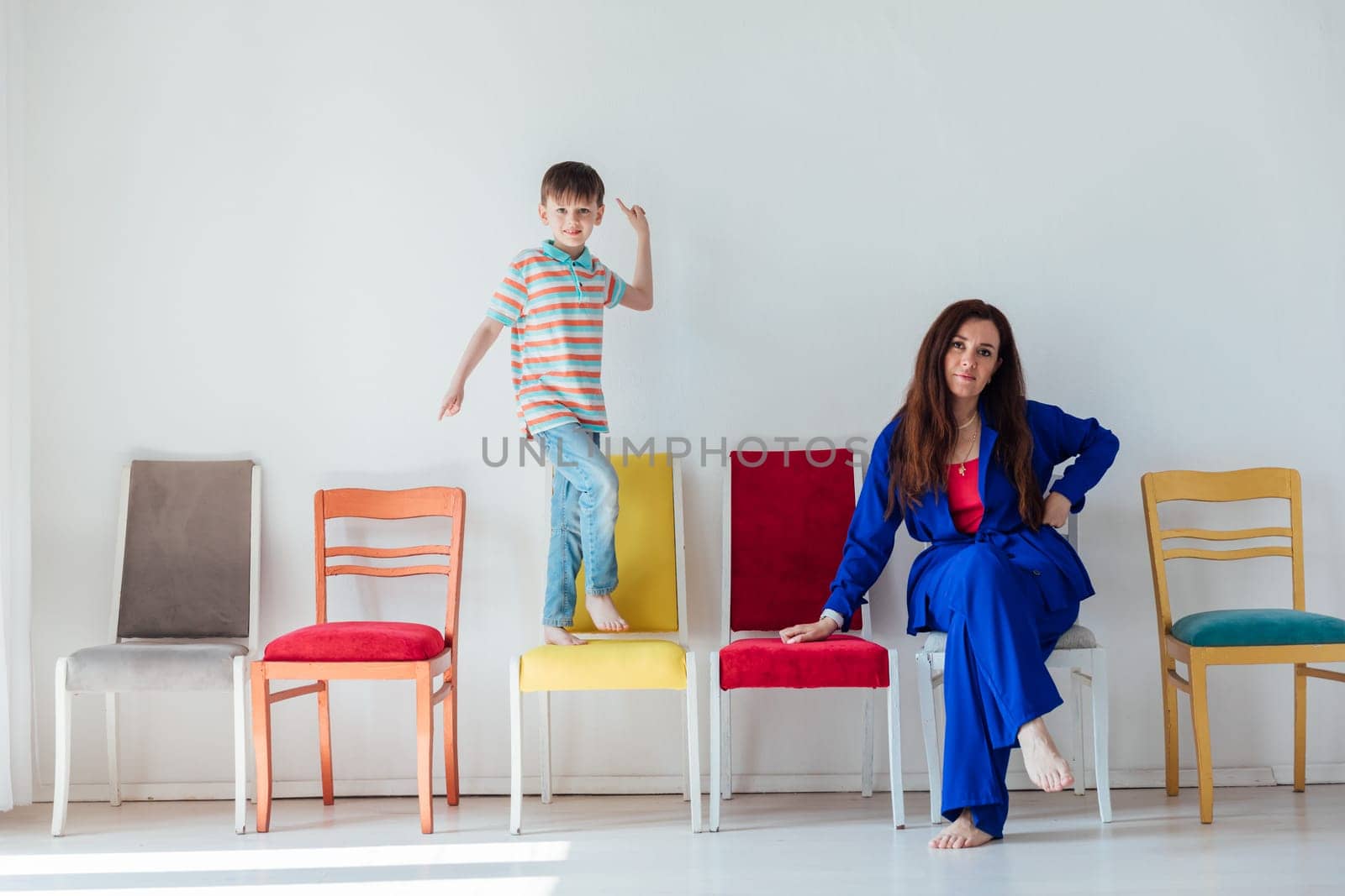Boy and woman and many different chairs in the interior of a white room