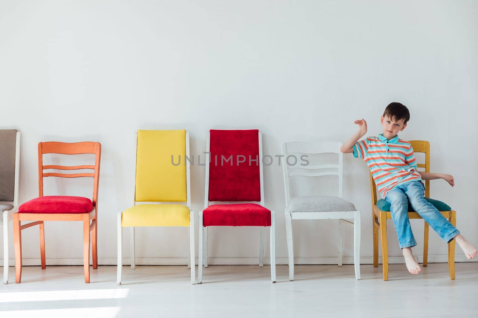 A 7-year-old boy and many different chairs in the interior of a white room