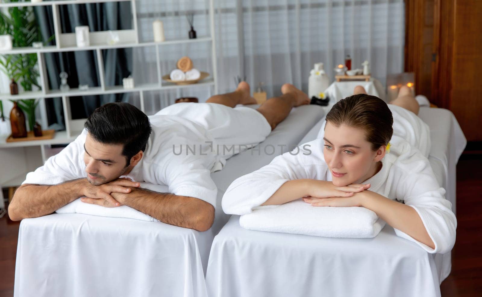 Caucasian couple customer enjoying relaxing anti-stress spa massage and pampering with beauty skin recreation leisure in day light ambient salon spa at luxury resort or hotel. Quiescent