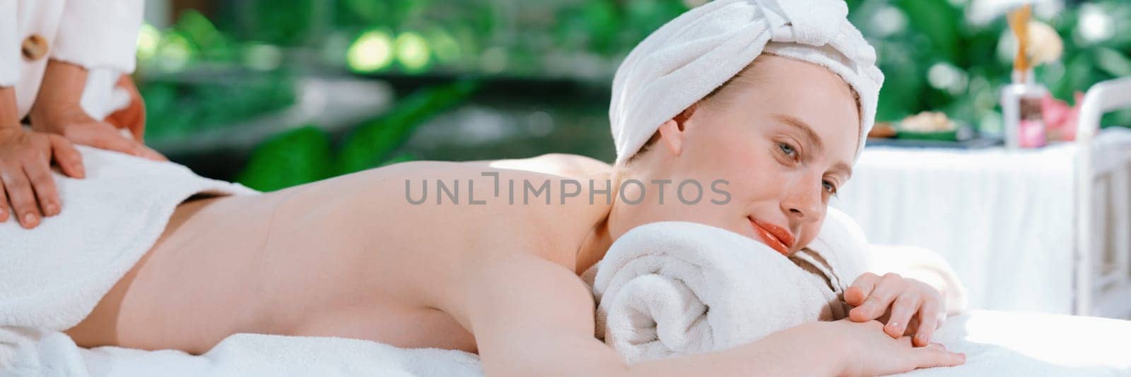 Beautiful young woman lies on white spa bed during having back massage. Attractive caucasian woman having back massage surrounded by natural environment. Relaxing and healthy concept Tranquility.