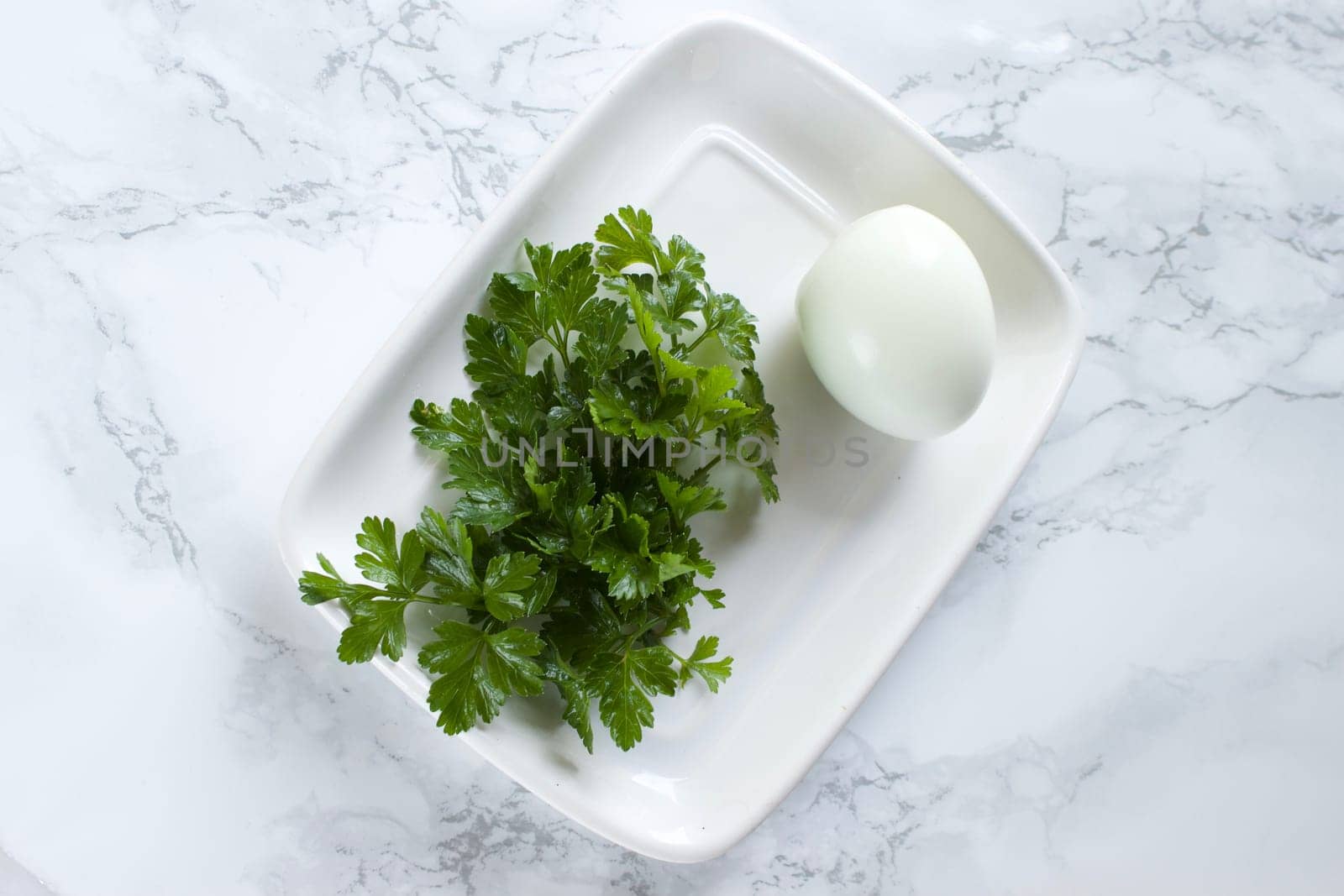 Boiled chicken egg and parsley on a white plate on a marble background. High quality photo
