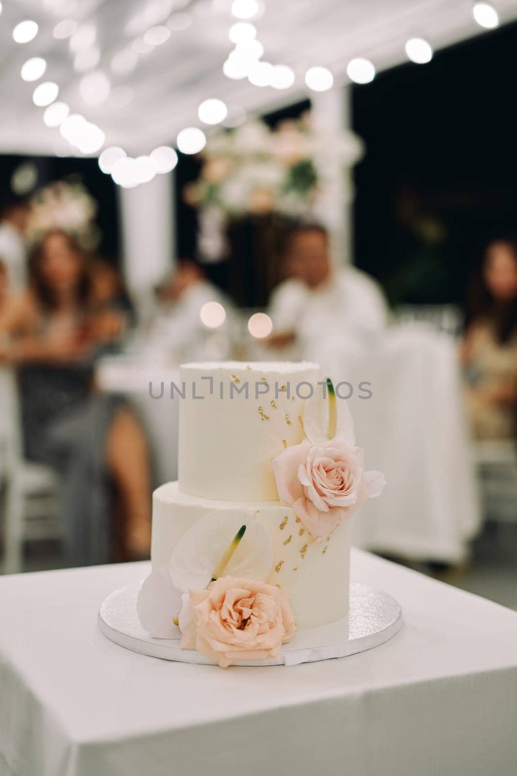 Wedding cake decorated with flowers stands on a tray on the table by Nadtochiy