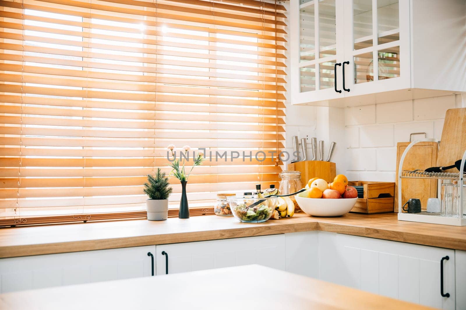 With wooden furniture and grey design tiles, this modern kitchen features a big window and a plant, creating a cozy Scandinavian interior. The clean and luxurious room is in white.