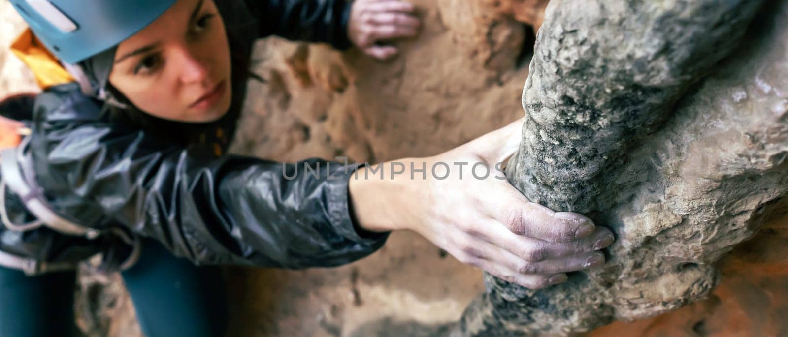 Young girl is engaged in extreme sports, fearlessly climbs up the rock using white magnesia powder, holds her hand to the ledge in the relief, close-up view, focus on the finger, the girl is blurred.