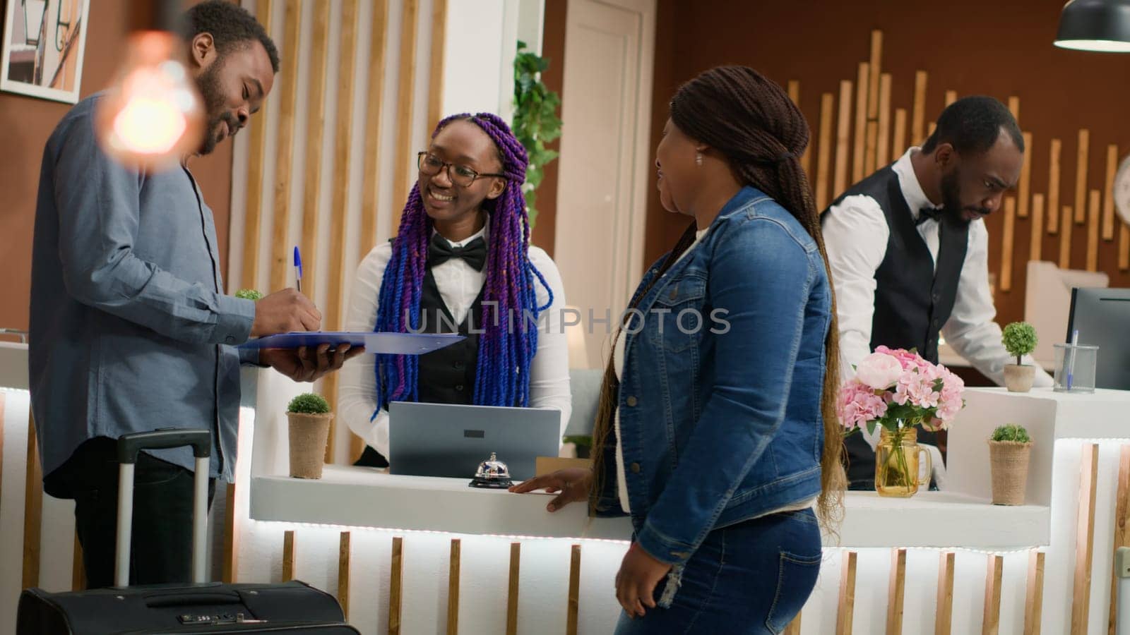 Front desk staff assisting at check in, helping hotel guests to relax with room reservation after long flight. Young couple receiving excellent concierge service at five star resort. Handheld shot.