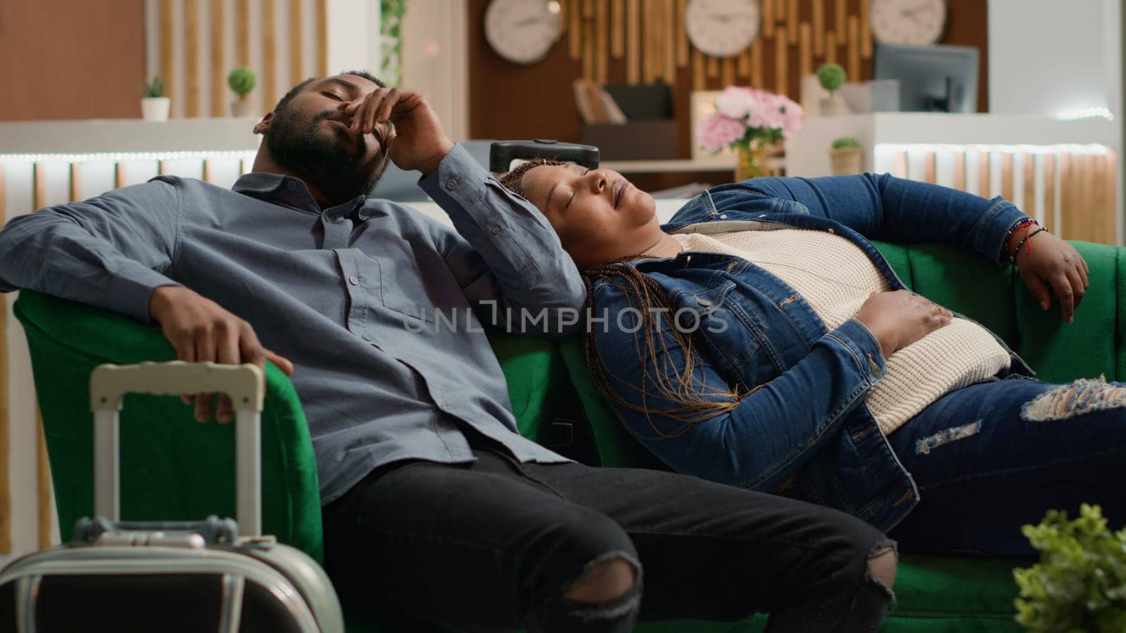 Tired sleepy couple sleeping on couch in hotel lobby, feeling exhausted after long flight. Unhappy african american tourists waiting for room check in, jet lag disorder symptoms. Handheld shot.