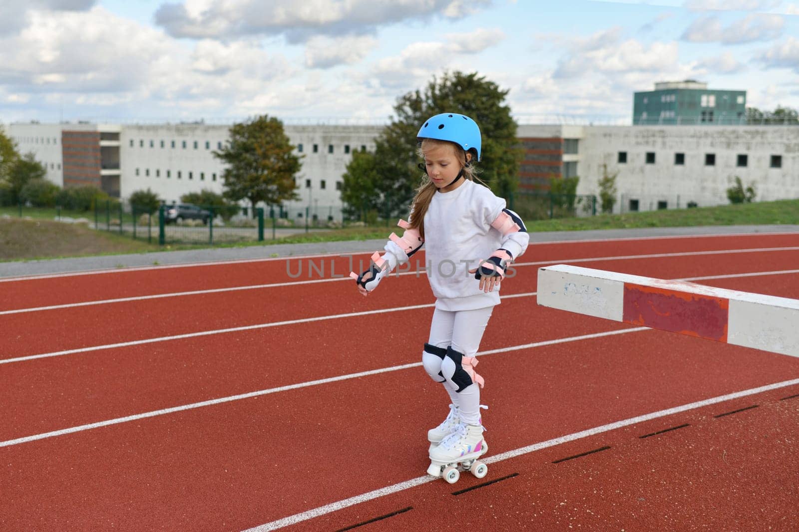 A girl in vintage white roller skates and a helmet at the stadium by Godi