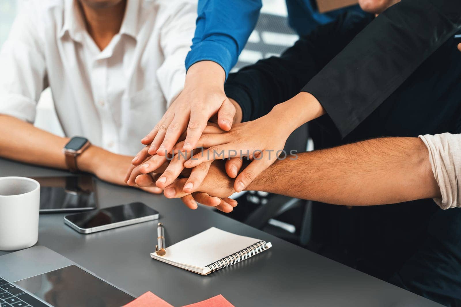 Group of diverse office worker join hand together in office room symbolize business synergy and strong productive teamwork in workplace. Cooperation and unity between business employee. Prudent