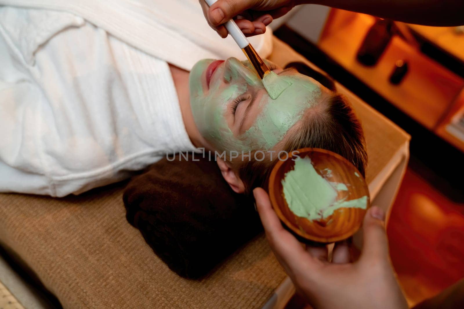 Serene ambiance of spa salon, woman customer indulges in rejuvenating with luxurious face cream massage with warm lighting candle. Facial skin treatment and beauty care concept. Quiescent