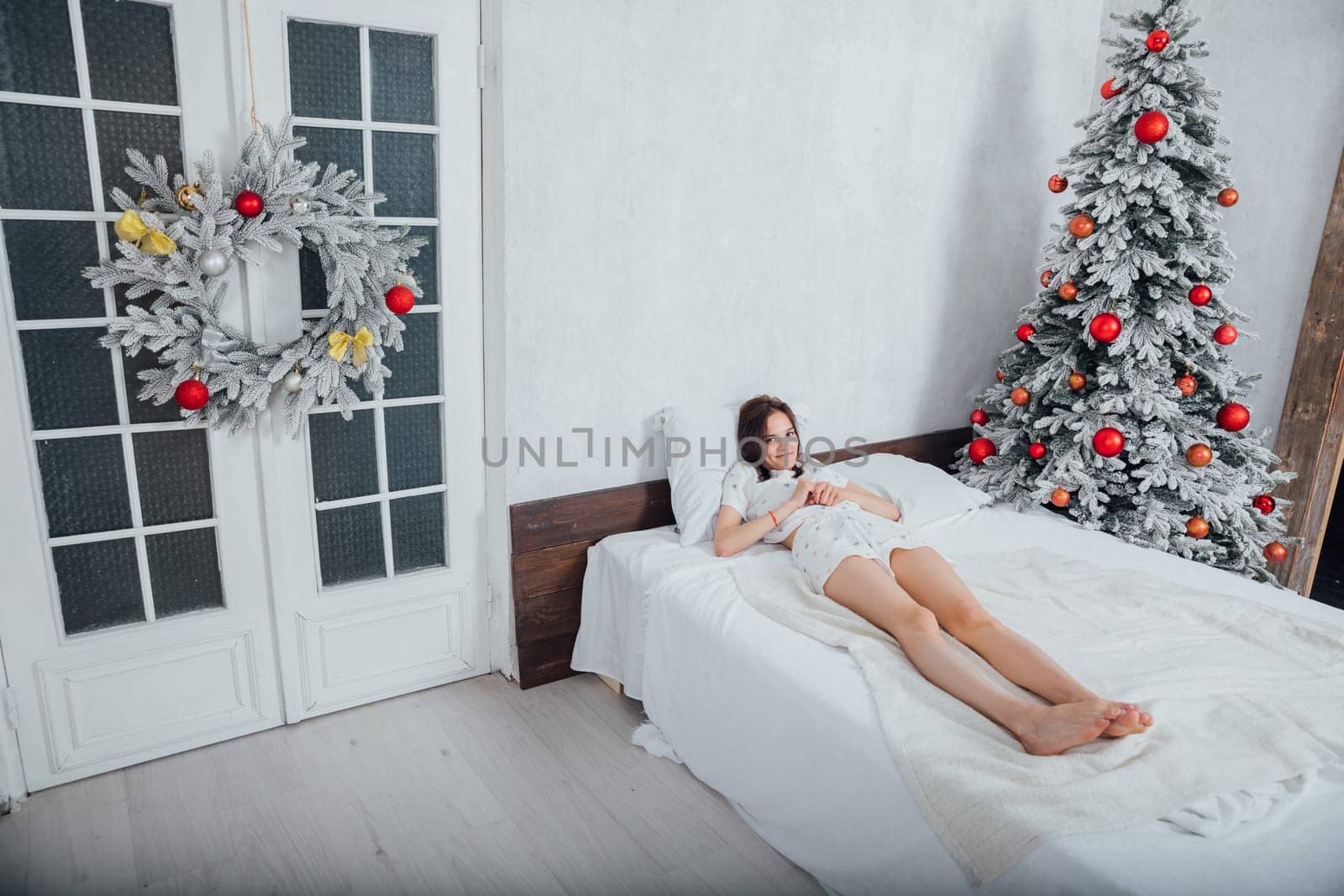 Woman lying on bed near christmas tree with gifts