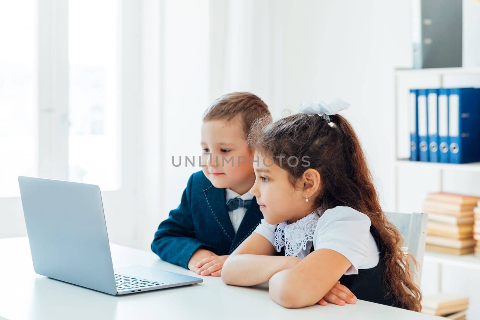 Boy and girl sitting at desk with laptop by Simakov