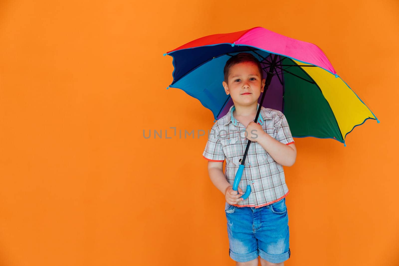 Little boy with colorful umbrella on orange background by Simakov