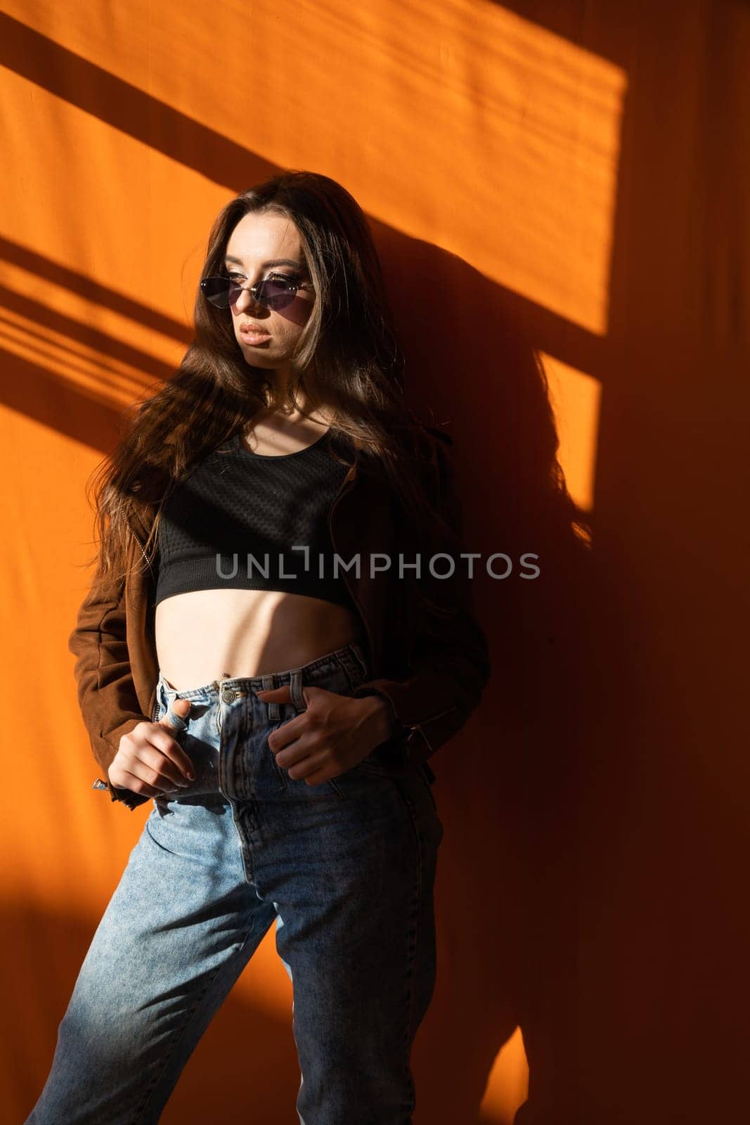 brunette with sunglasses standing on an orange background in sunset light