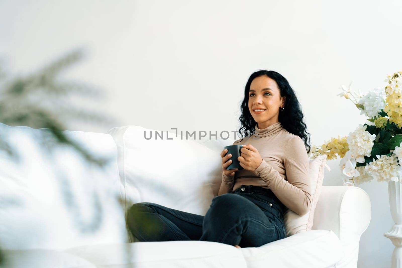 Happy woman drinking coffee on a sofa at home for crucial rest and relaxation. Portrait of young African American woman holding a cup.