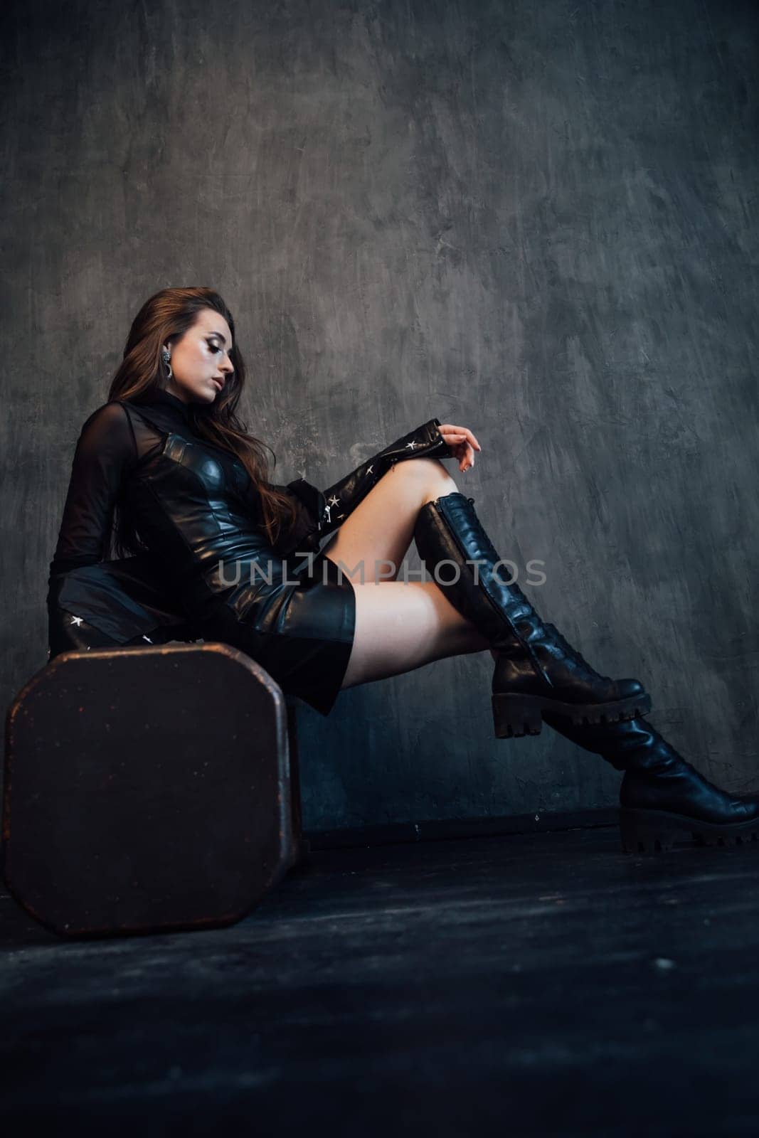 brunette in leather clothes in a dark room on a gray background near the chest