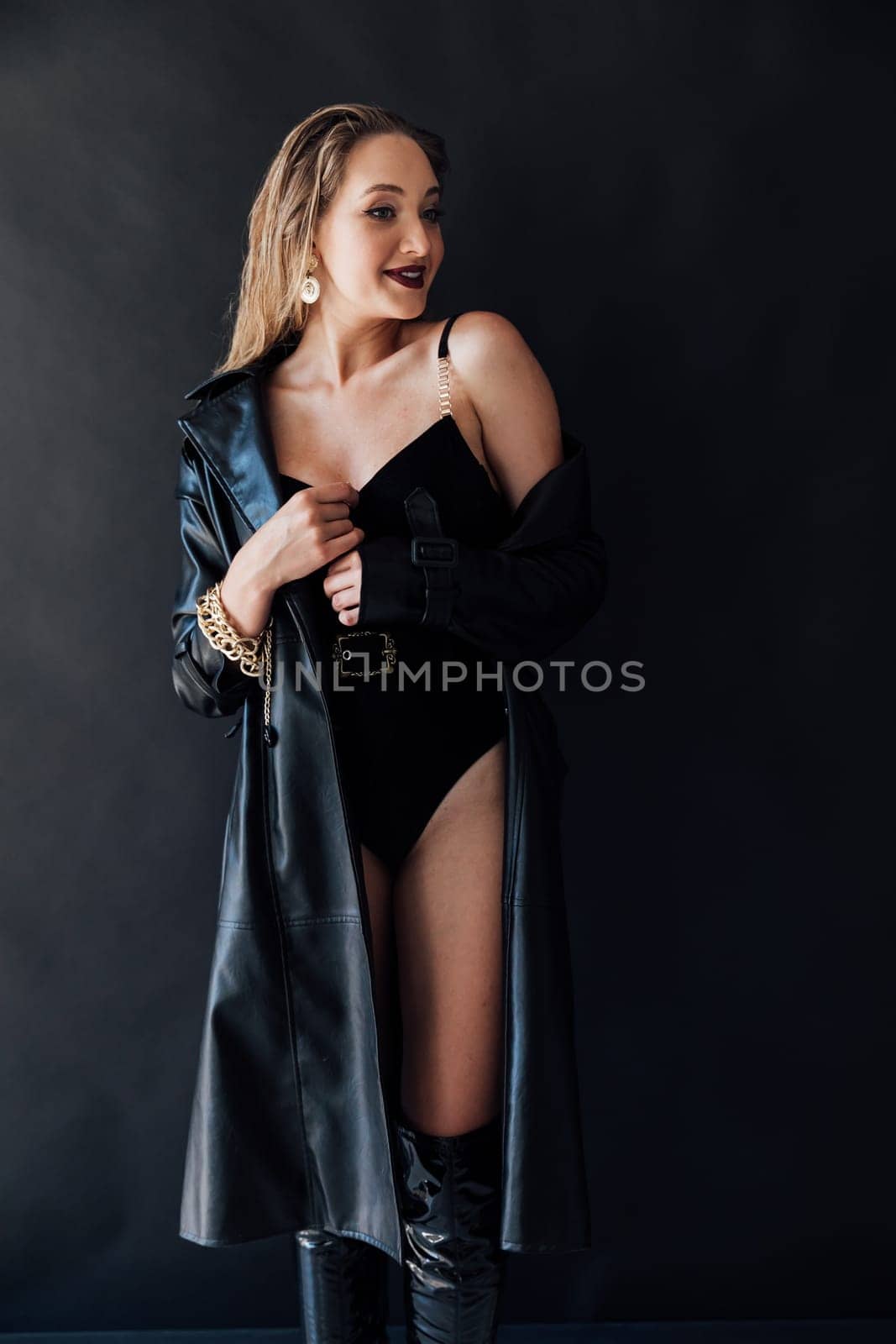 a femme fatale in black clothes poses on a black background in a dark room