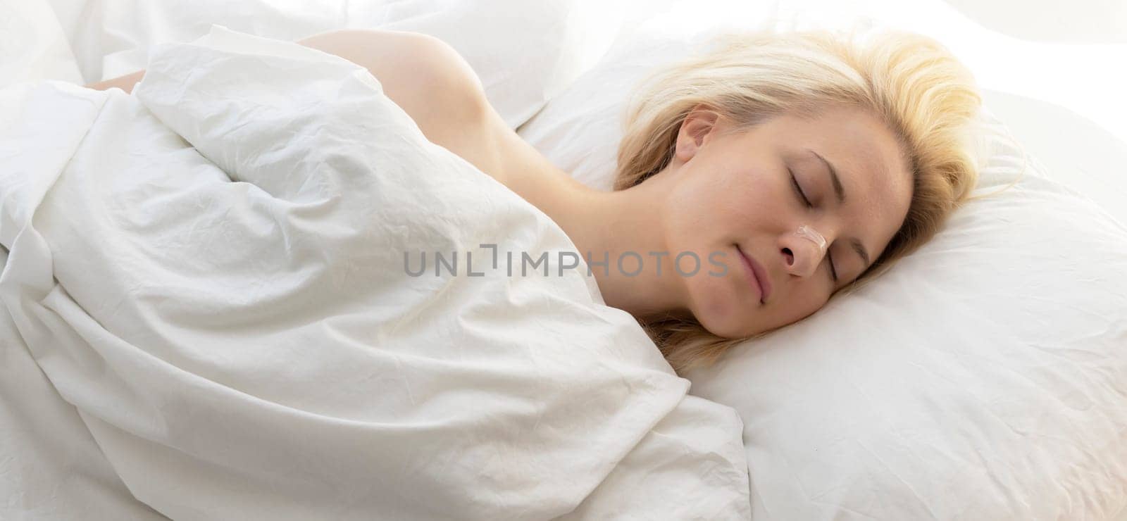 Woman Sleeping In Bed With Nasal Strip On Nose On White Linen. Stop Drug-free Snoring Solution. Adhesive Bandage For Better Healthy Breathing. Horizontal Plane. Female Takes Calm Sleep Every Night.