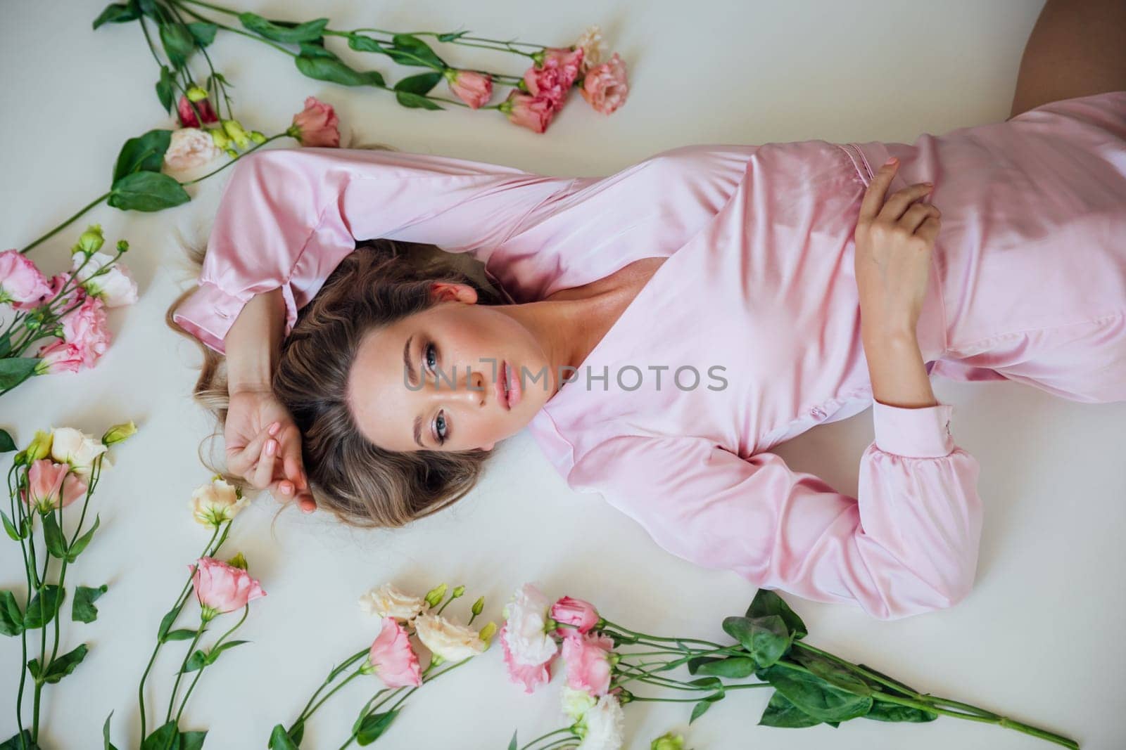 a blonde lies in flowers in a bright room