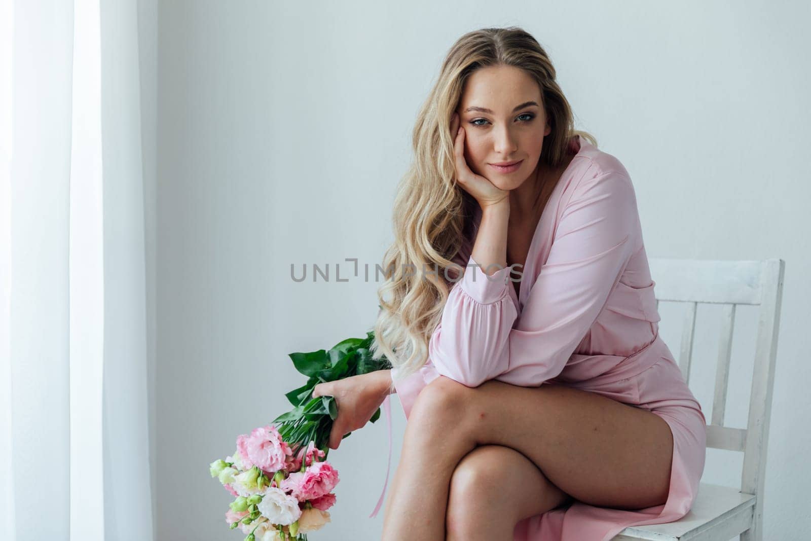 a blonde sits with flowers on a white background in a bright room