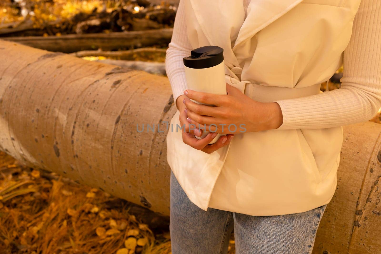 Caucasian Female Drinks Autumn Beverage From Thermos, Travel Mug Outside In Park Or Forest, Wears Warm Beige Vest. Hot Tea Or Coffee, Fall Leaves Season. Horizontal Plane Yellow background. Copyspace.
