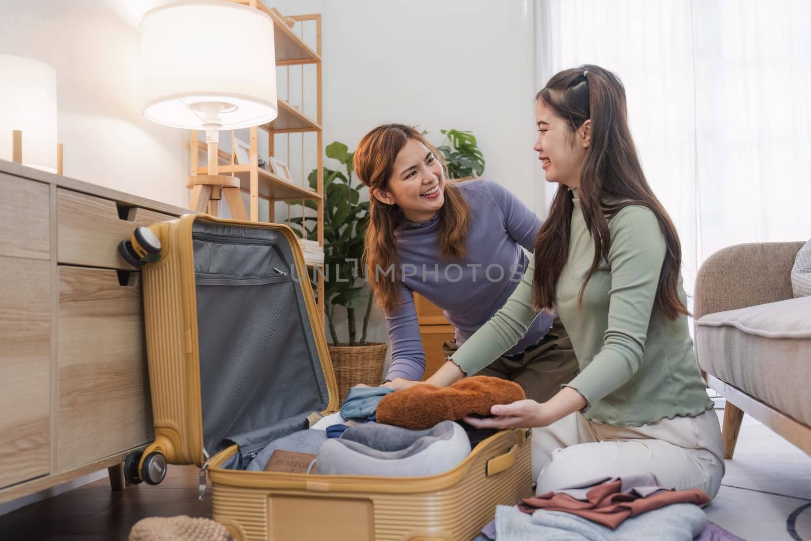Young Asian woman packs clothes into a suitcase. Preparing for the summer vacation Two women are planning a trip and helping prepare their suitcases for a trip abroad. by wichayada