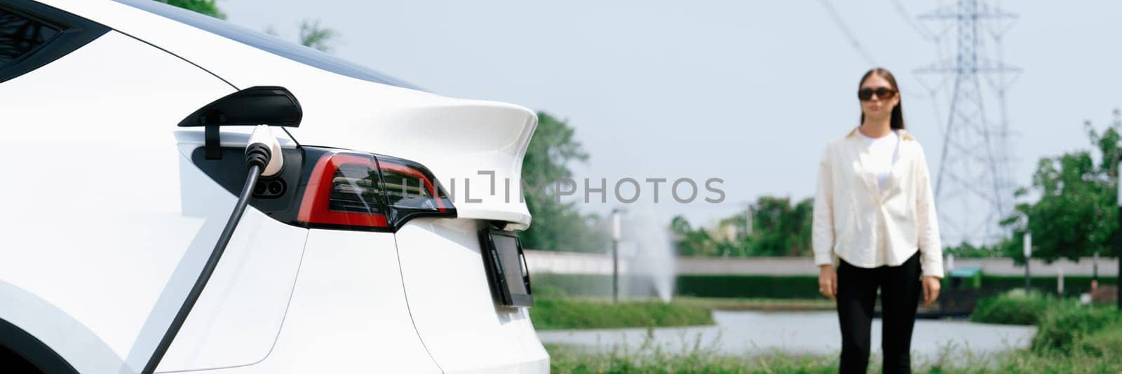 Young woman recharge EV car battery at charging station. Expedient by biancoblue