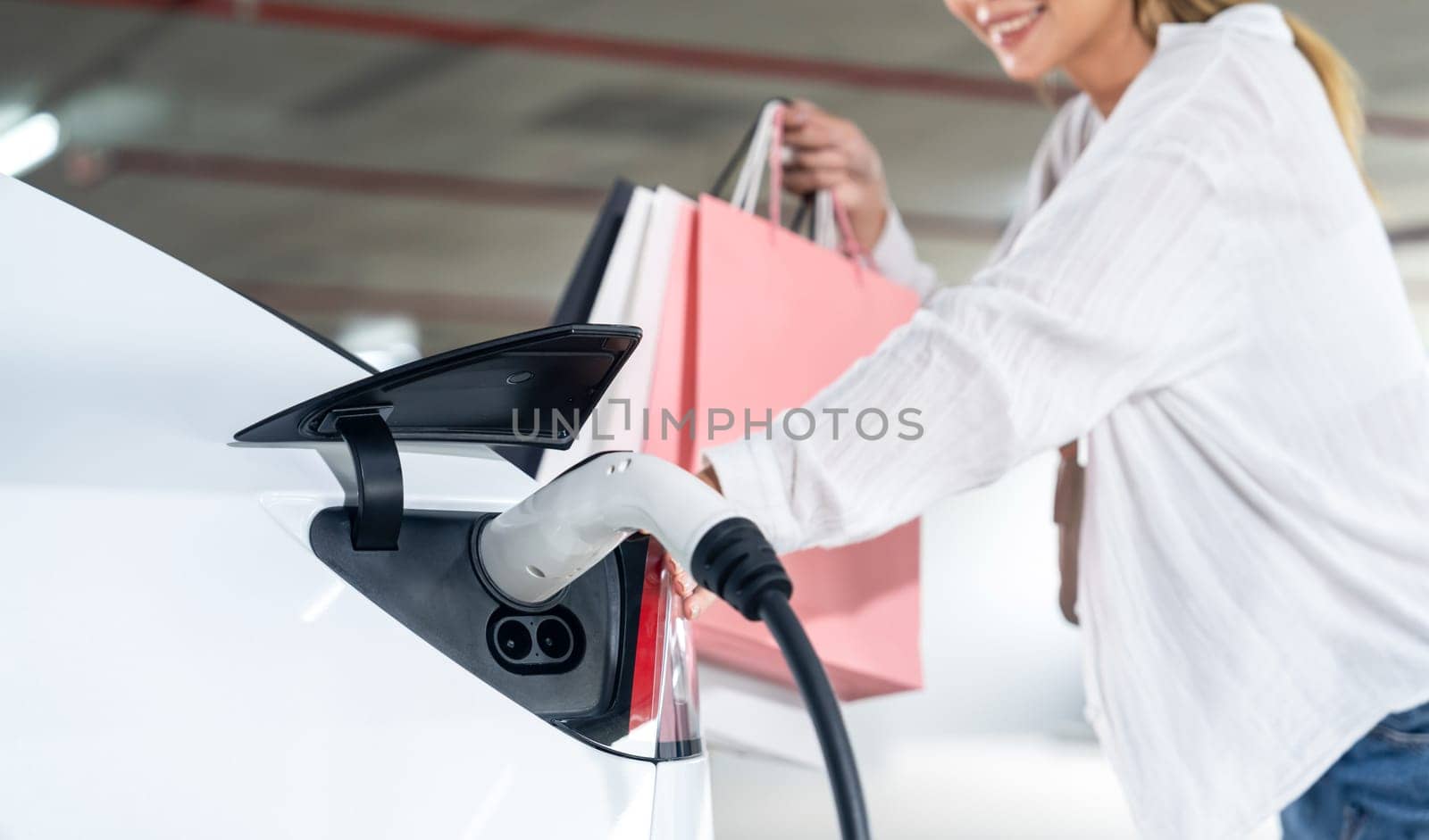 Young woman travel with EV electric car to shopping center parking lot charging in downtown city showing urban sustainability lifestyle by green clean rechargeable energy of electric vehicle innards