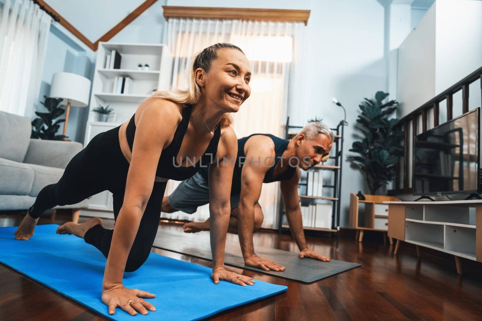 Athletic and active senior couple doing exercise on fit mat with plank climbing together at home exercise as concept of healthy fit body lifestyle after retirement. Clout