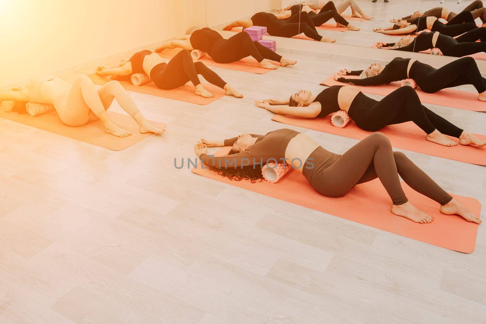 Group of young womans fitness instructor in Sportswear Leggings and Tops, stretching in the gym before pilates, on a yoga mat near the large window on a sunny day, female fitness yoga routine concept.