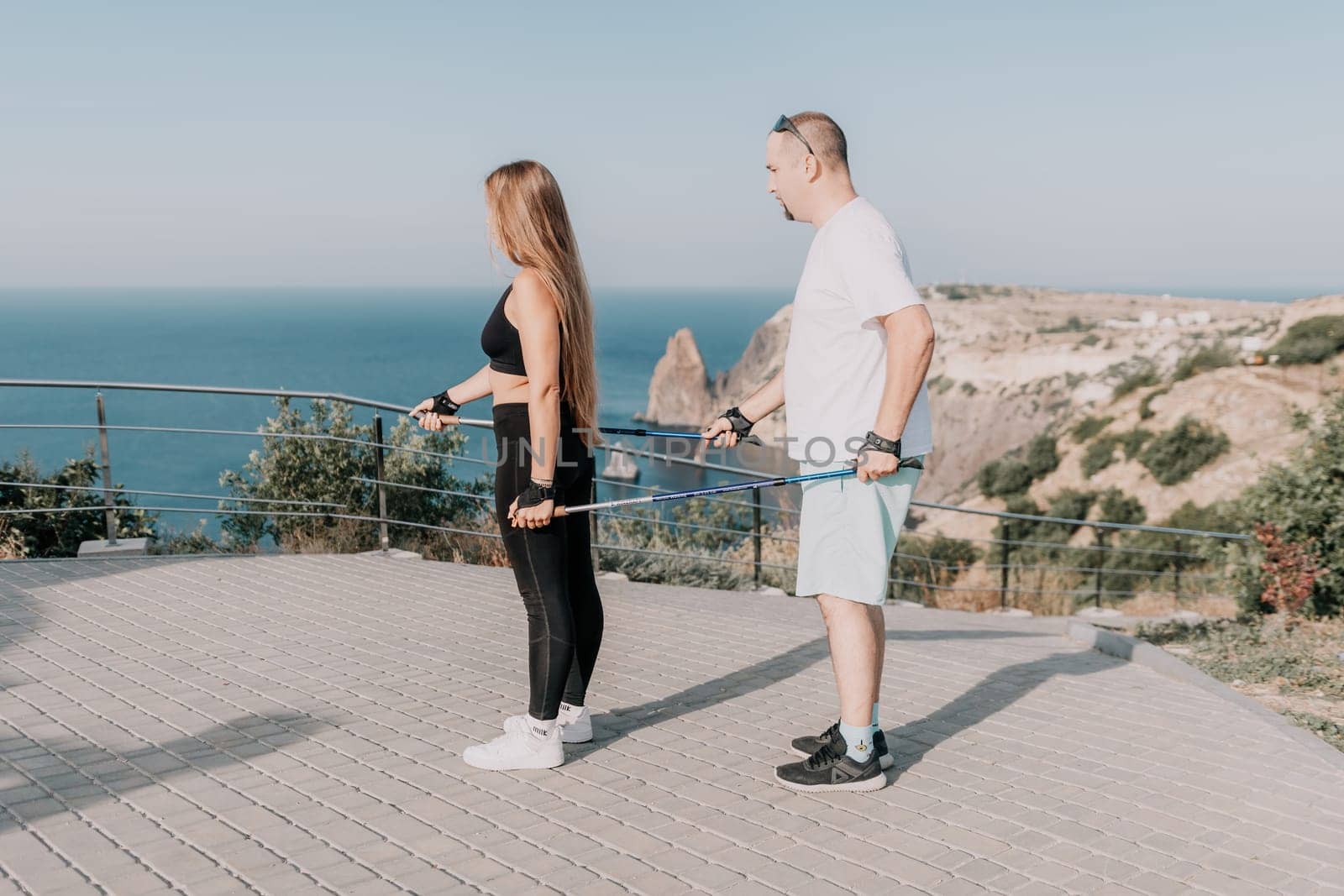 Happy Middle aged couple or friends practicing nordic walking in park near sea. Mature couple with trekking poles walking, practicing Nordic walking outdoors. Aging youthfully and sport concept.