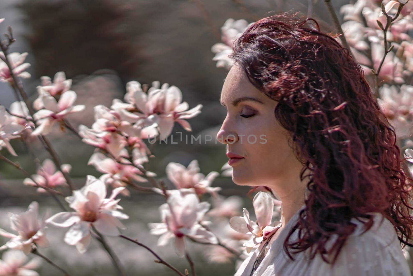 Magnolia park woman. Stylish woman in a hat stands near the magnolia bush in the park. Dressed in white corset pants and posing for the camera. by Matiunina