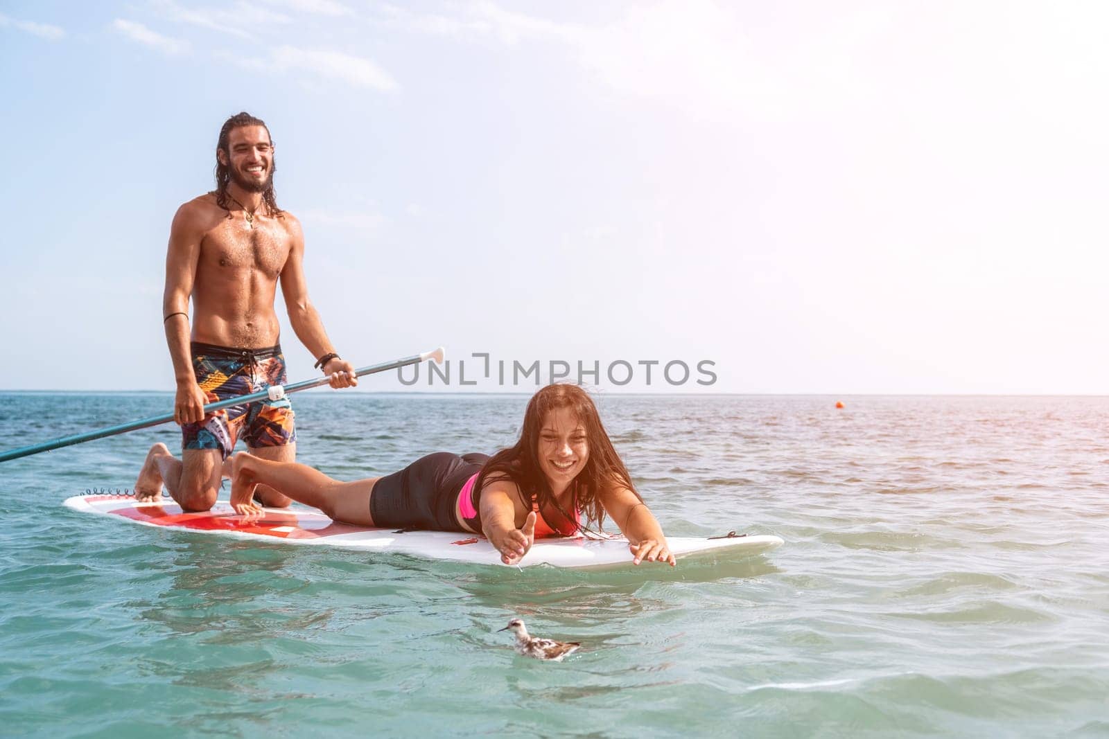 Silhouette of woman standing, surfing on SUP board, confident paddling through water surface. Idyllic sunset or sunrise. Sports active lifestyle at sea or river.