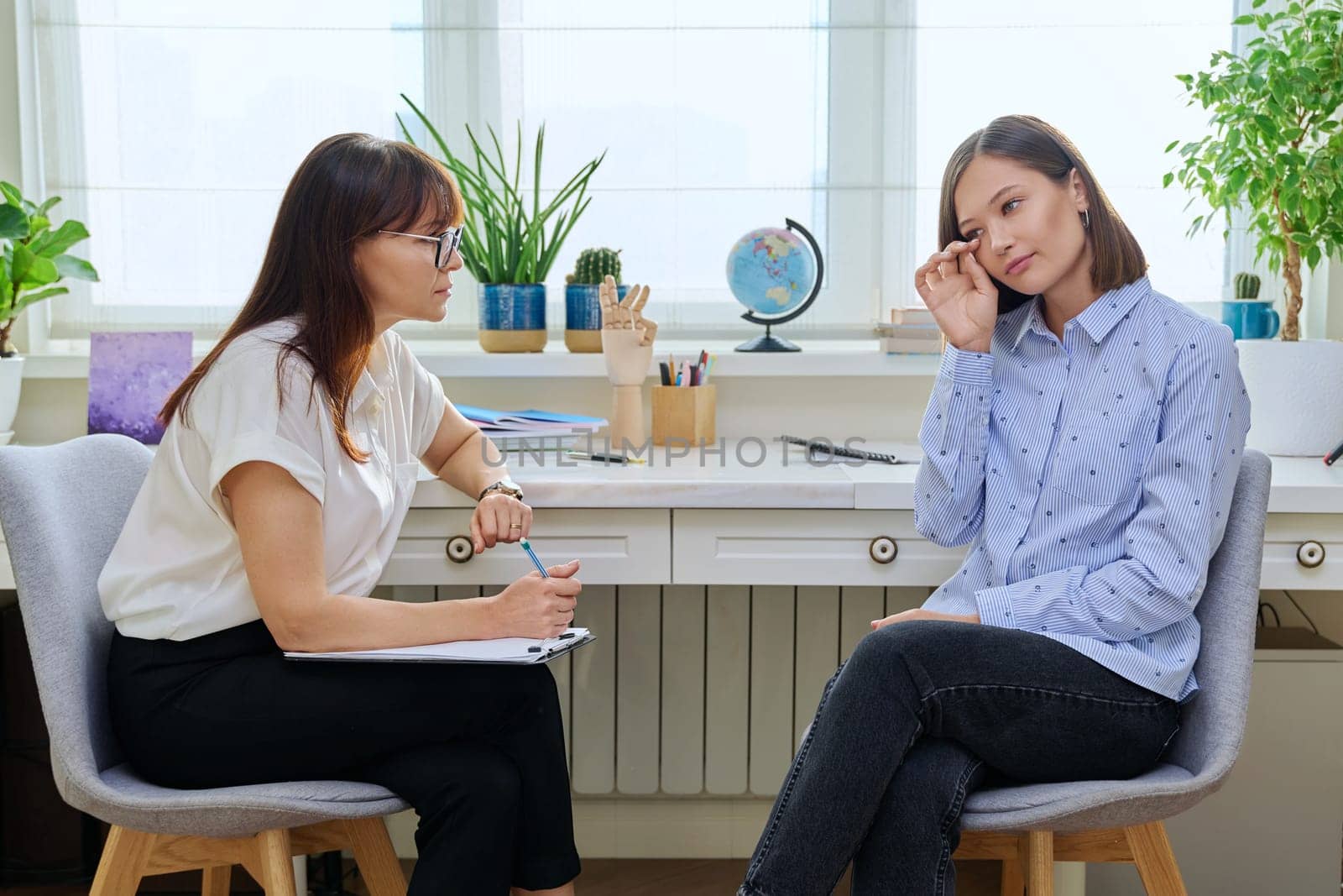 Sad stressed young woman in therapy with professional psychologist. Women talking in office, therapist counselor psychotherapist working with patient. Support, mental health, psychology, psychotherapy