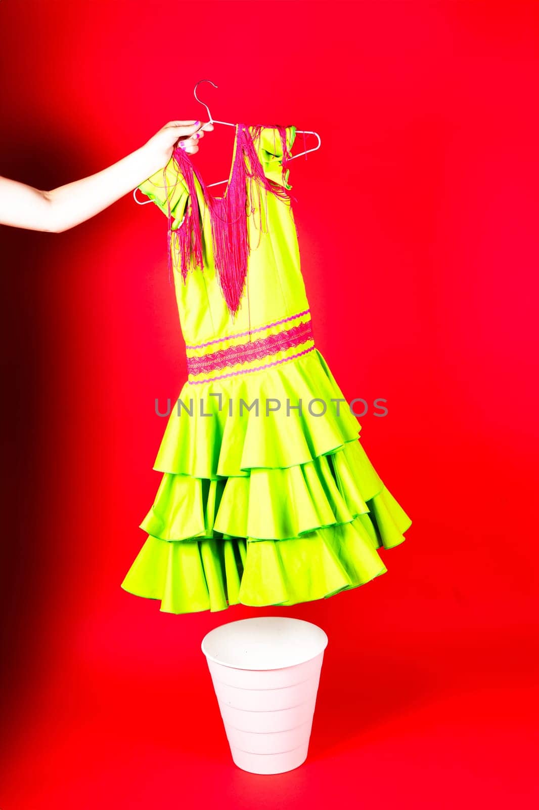 Shot of a young woman hand throwing her outwear dress in the trash isolated on red background by Zelenin