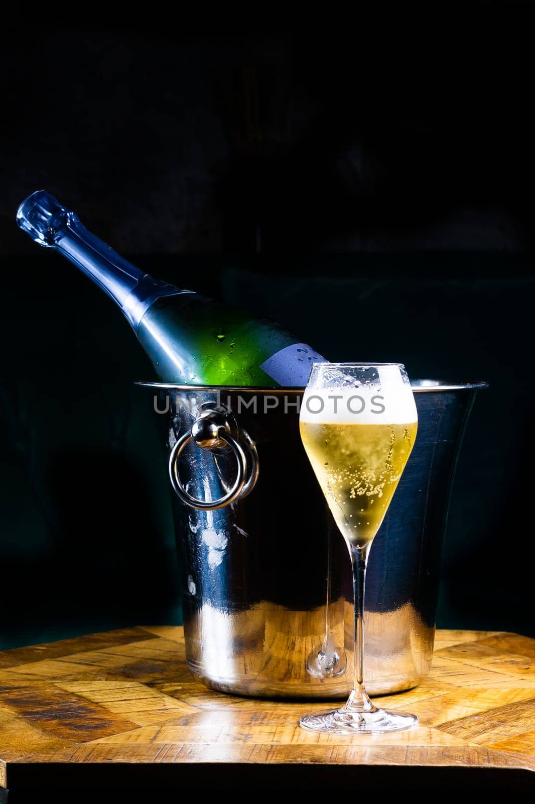 Bottle and cup of champagne on a wooden table, dark background